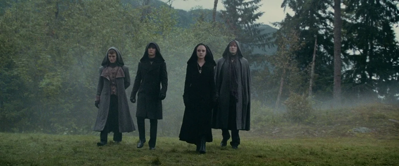 The Twilight Saga: Eclipse (2010) movie still: fullbody — Four people in dark hooded cloaks walk through a foggy, green clearing. Dense forest lines…
