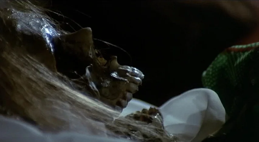 Lisa and The Devil (1973) movie still: closeup — A human skull lies on white fabric within a dark, enclosed stone space. Wisps of hair are matted…