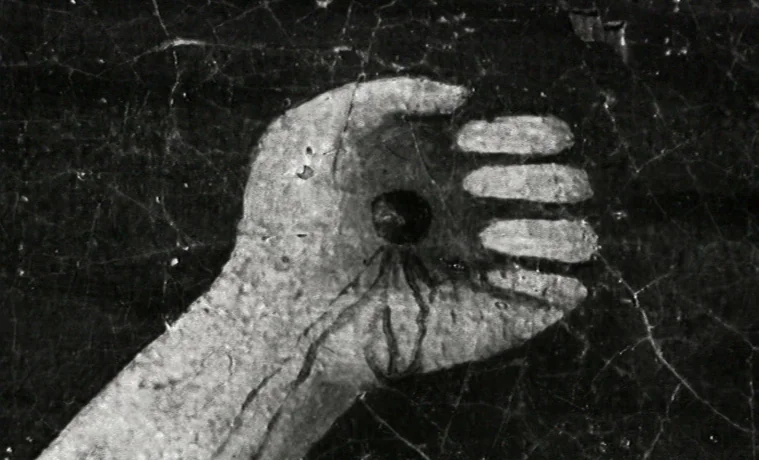 The Garden (1990) movie still: closeup — A close-up of a textured, white-painted hand on a cracked, dark surface. The fingers are extended…