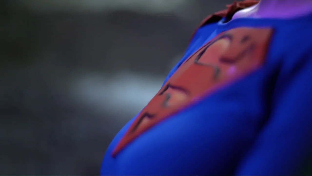 Reign of the Superwomen (2021) movie still: closeup — A close-up view focuses on the chest of a blue and red superhero costume. The textured fabric…