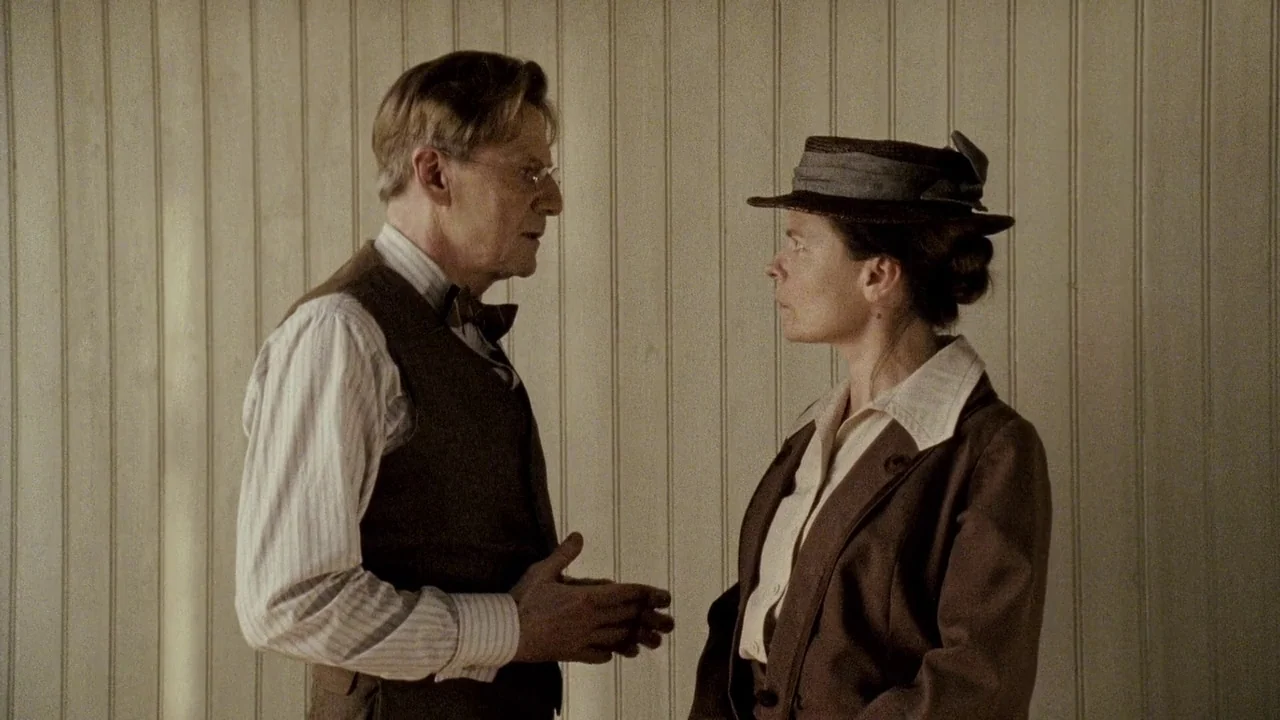 Everlasting Moments (2008) movie still: medium — An interior space features vertical wooden paneling on the wall behind two people. A man in a vest…