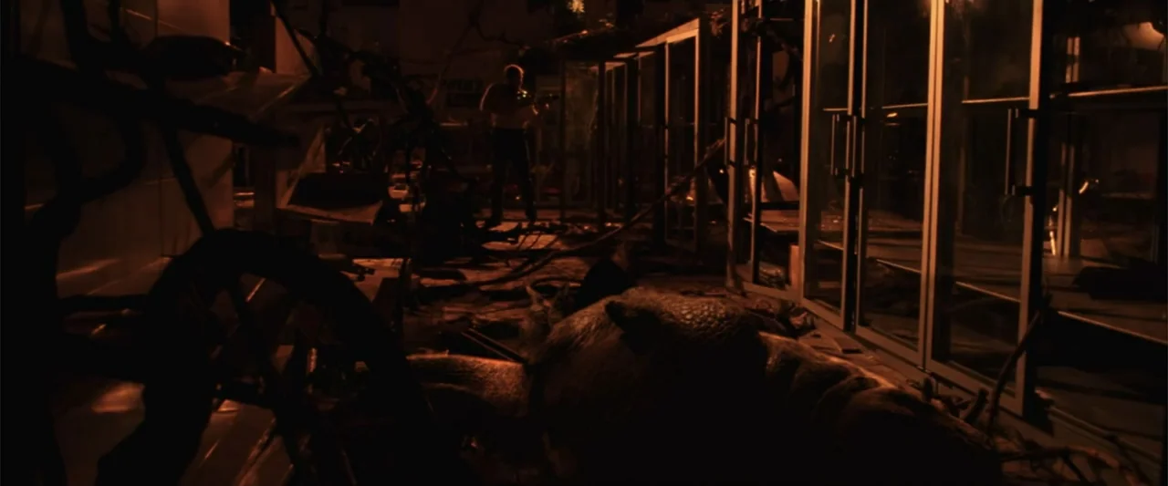 A Sound of Thunder (2005) movie still: wide — A dark indoor area features large glass display cases and scattered debris on the floor. A man stands…