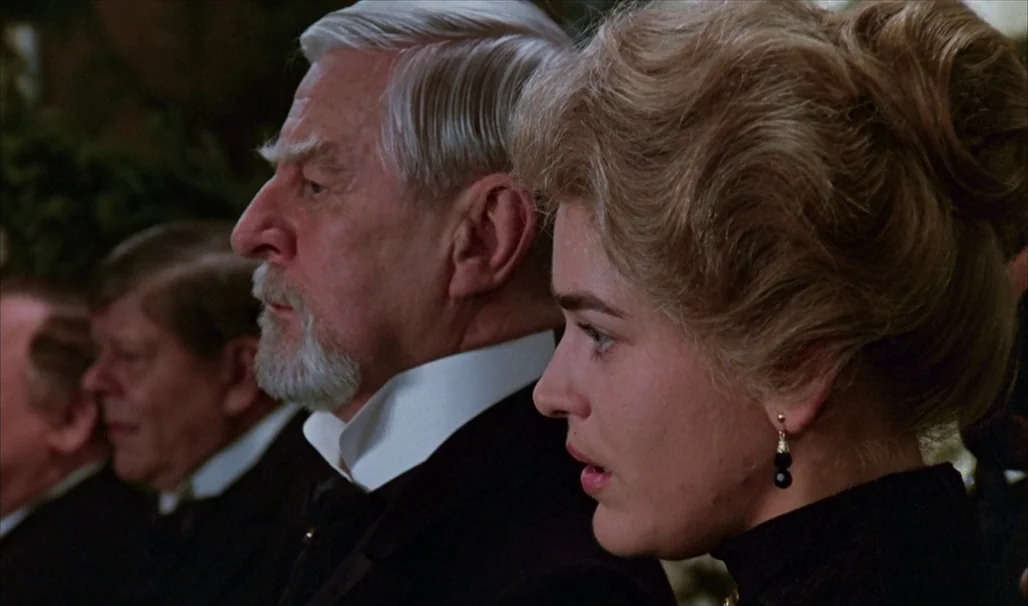 Fanny and Alexander (1982) movie still: medium — Two individuals sit together in dark formal attire within a dimly lit interior space. A young woman…