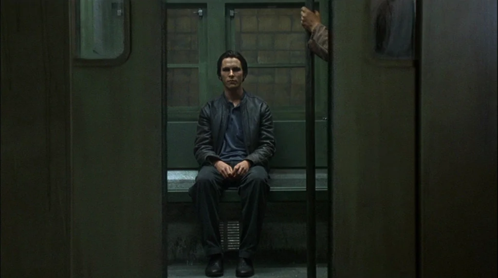 Velvet Goldmine (1998) movie still: medium — A dark subway car interior with green seating and a vertical metal handrail. A lone man sits centered…