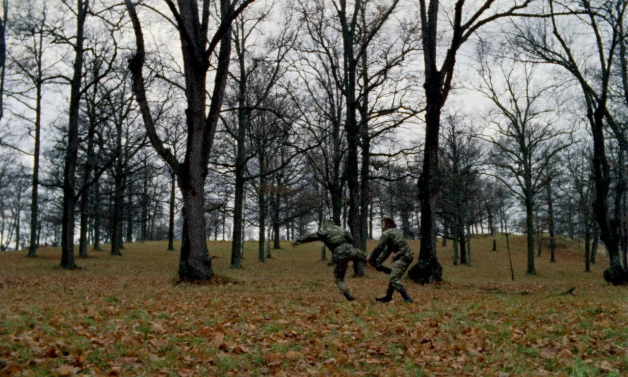 Thriller: A Cruel Picture (1973) movie still: wide — A clearing in a dense, leafless deciduous grove with a thick carpet of fallen leaves. Two…
