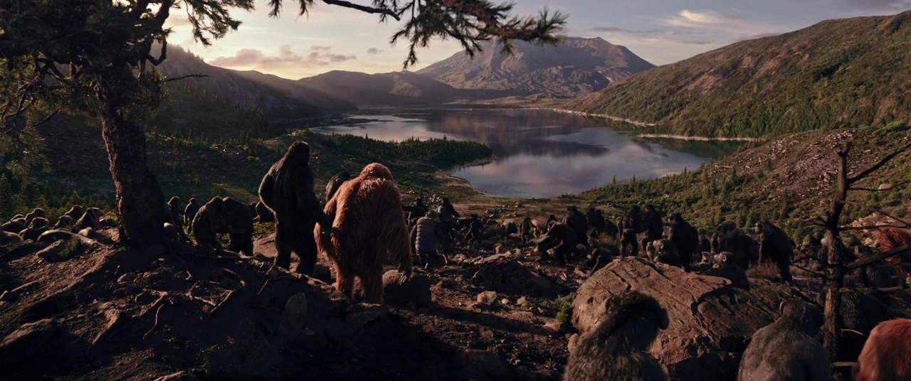 War for the Planet of the Apes (2017) movie still: wide — A group of primates traverses a rocky, tree-lined hillside overlooking a vast calm lake.…
