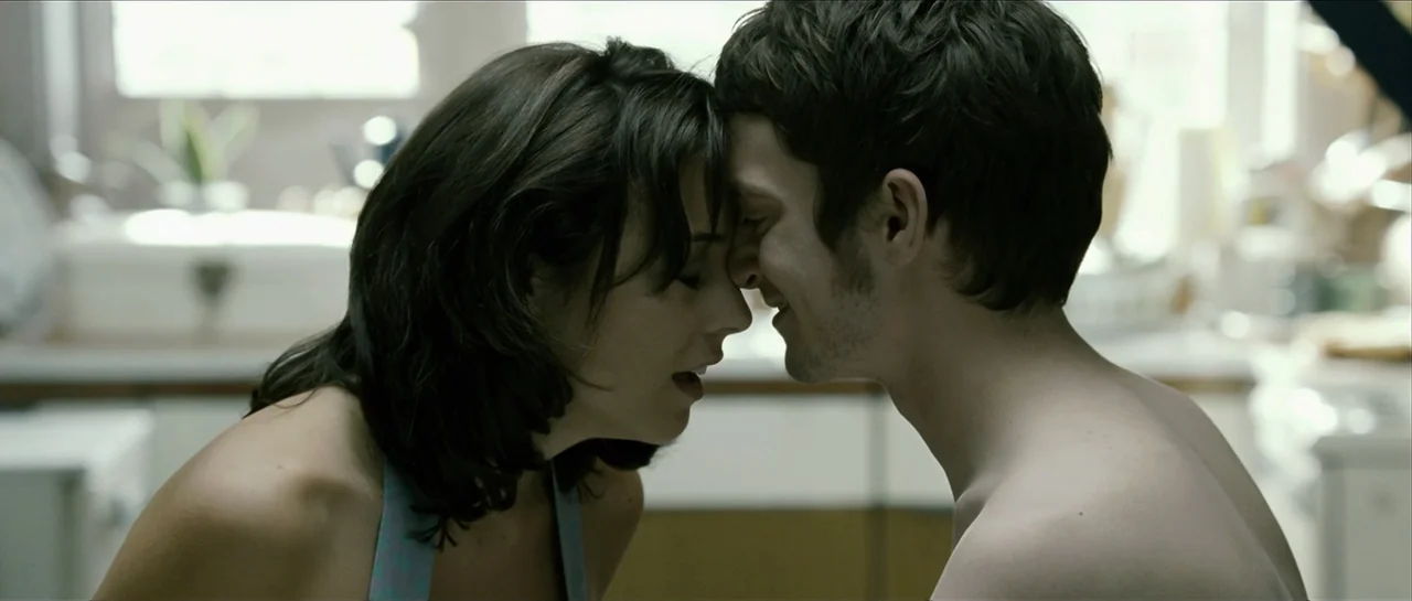 The Oxford Murders (2008) movie still: medium — A sunlit kitchen interior with blurred white cabinetry in the background. A young man and woman face…