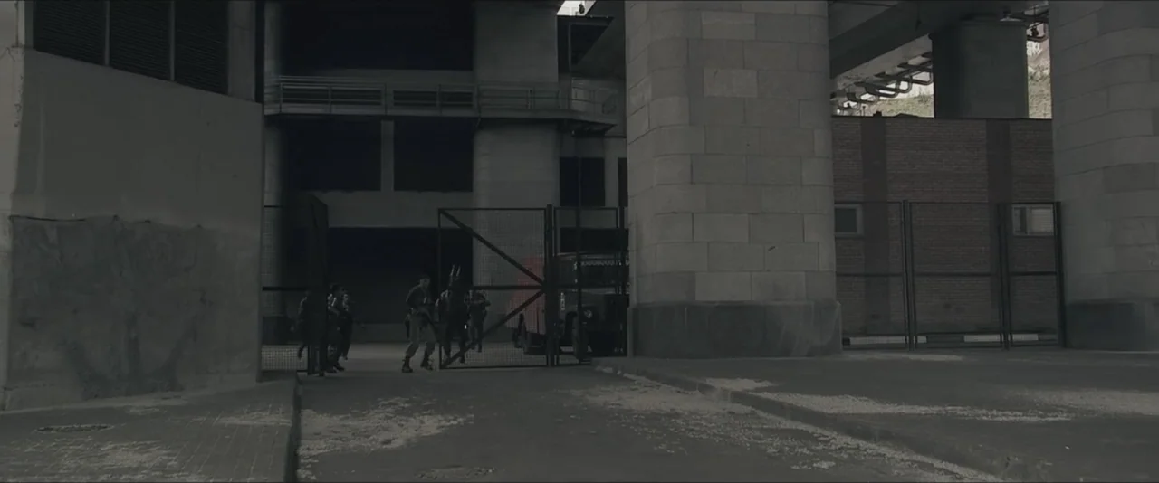 Darkest Hour (2017) movie still: wide — A concrete underpass features large supporting pillars and a tall metal gate entryway. Soldiers in tactical…