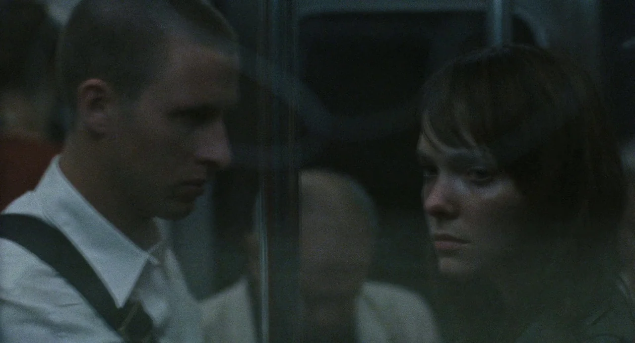 Reprise (2006) movie still: medium — A dark, dimly lit subway car interior at night with reflective glass surfaces. A man and a woman stand…