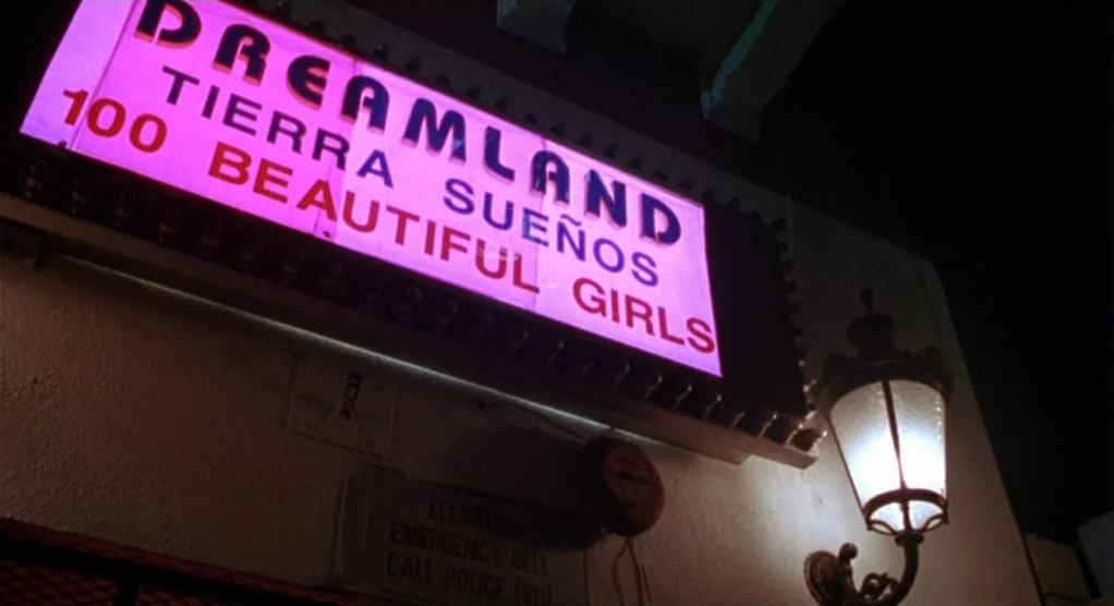 The Crossing Guard (1995) movie still: medium — A neon sign labeled Dreamland hangs above an emergency call box on an exterior wall. The sign…