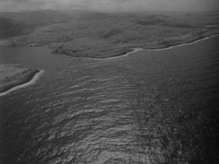 I Am Cuba (1964) movie still: establishing — An aerial view shows a jagged coastline meeting a vast expanse of ocean water. Hilly land covered in…