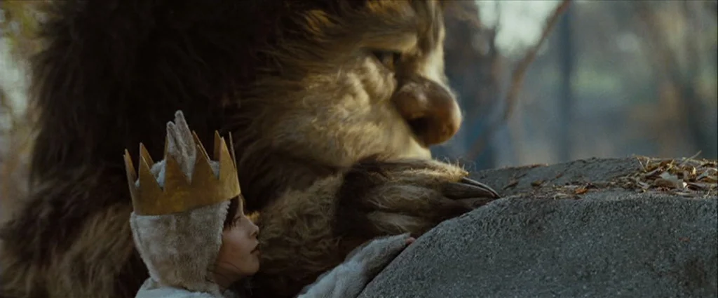Where The Wild Things Are (2009) movie still: medium — An outdoor area with a large grey rock and blurry vegetation in the background. A human child…