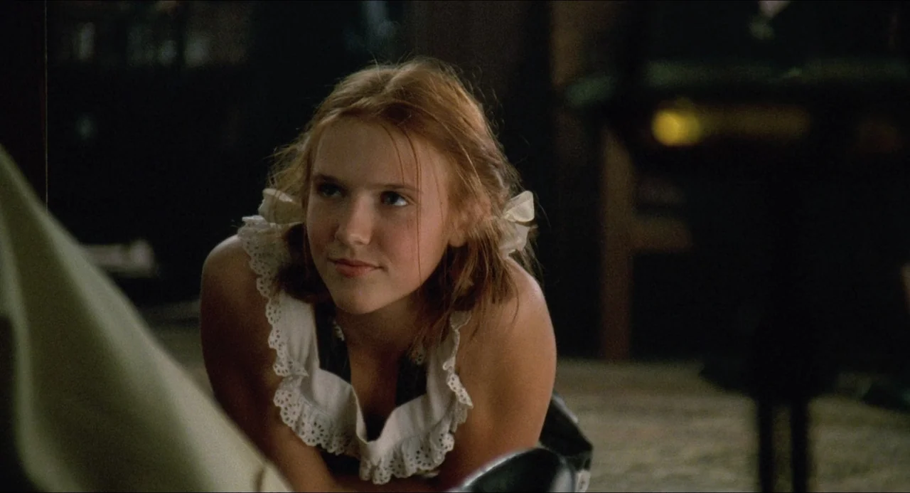 Lolita (1997) movie still: closeup — An interior space with a dark background and ambient light focused on the subject. A teenage girl with pigtails…