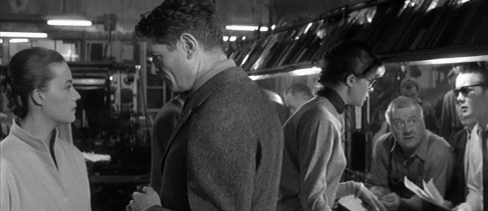 Les Amants (1958) movie still: medium — A busy industrial printing plant features metal machinery and overhead racks holding paper plates. A man in…