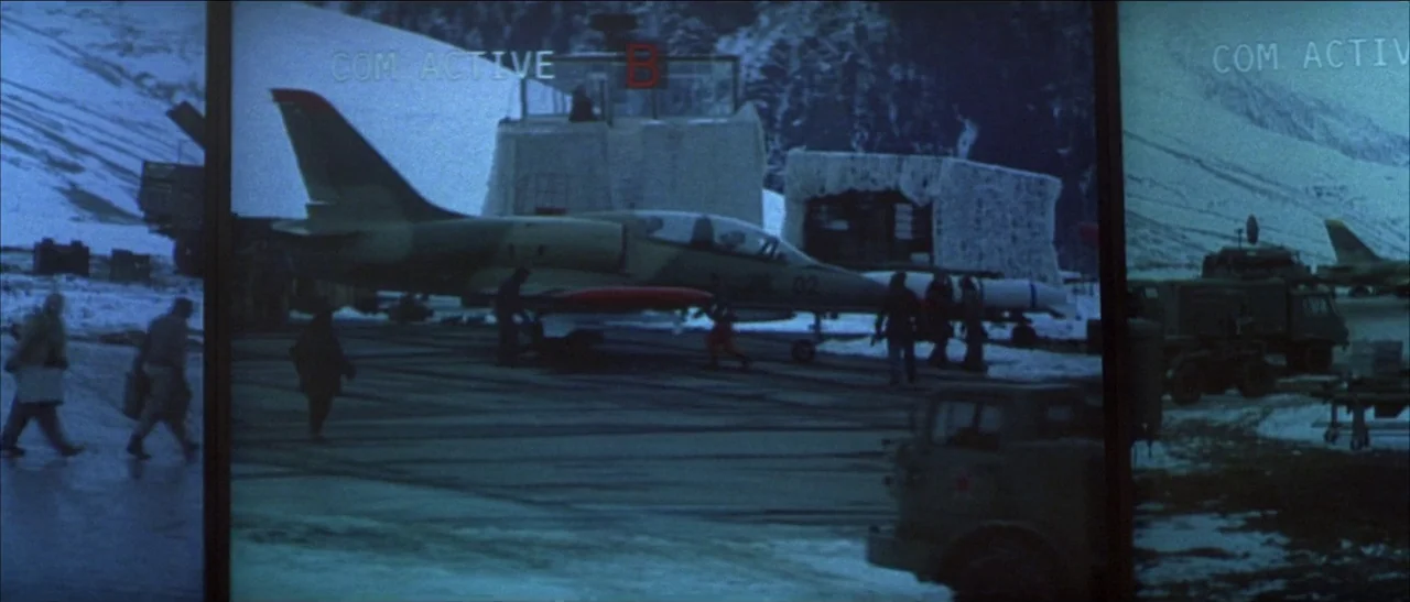 Tomorrow Never Dies (1997) movie still: wide — A snowy airfield features a parked jet aircraft on a dark concrete landing strip. Several figures…