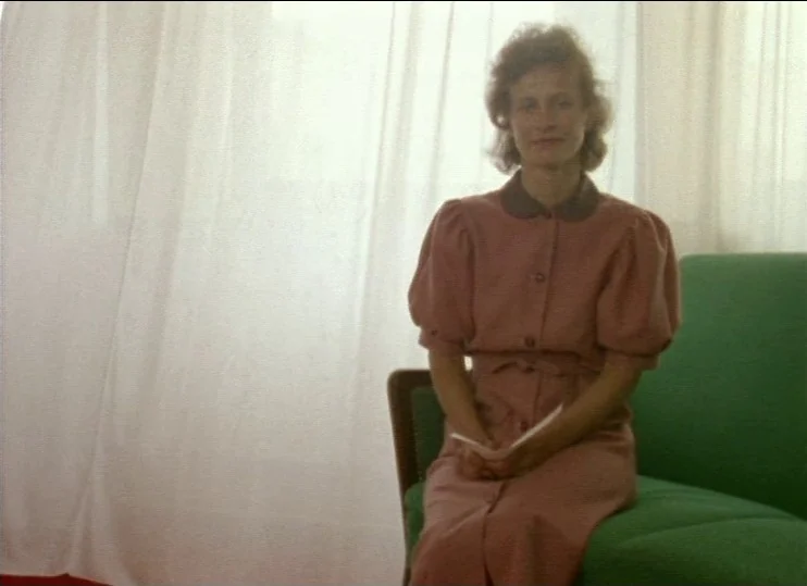 From The East (1993) movie still: medium — A woman sits in a room with light curtains filtering sunlight behind her. She sits on a bright green…