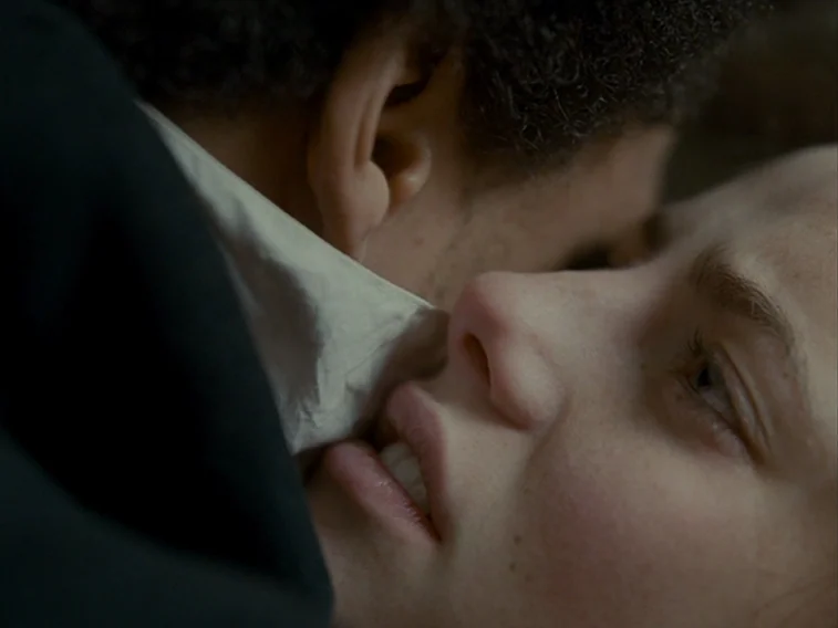 Wuthering Heights movie still: closeup — Two individuals are positioned close together in an interior residential space. One person presses their…