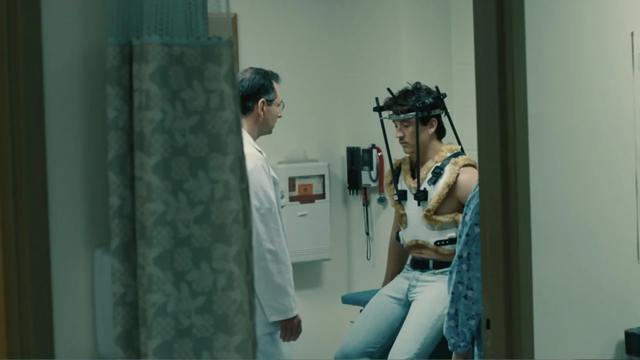 Bleed for This (2016) movie still: medium — A clinical examination room with beige walls and a mounted biohazard wall container. A man in a medical…