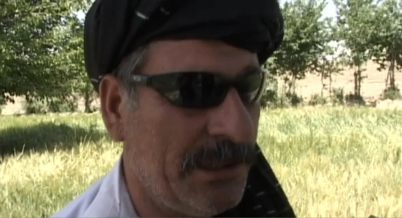 Afghanistan's Opium Trail (2007) movie still: closeup — A man stands outdoors in a bright green grain field. He wears a dark head covering and…
