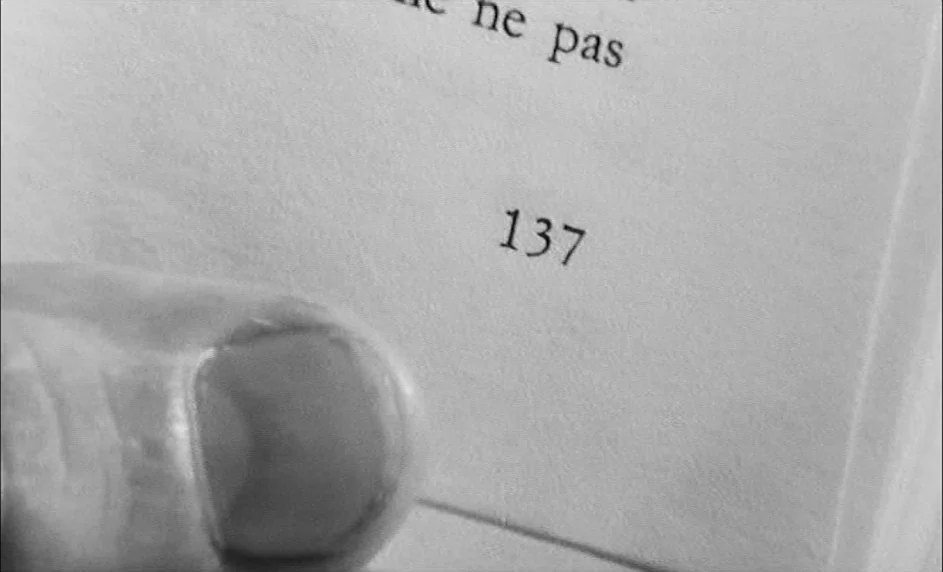 Boy Meets Girl (1984) movie still: closeup — A close-up of a page in an open book with the number 137 visible. A human thumb presses against the…