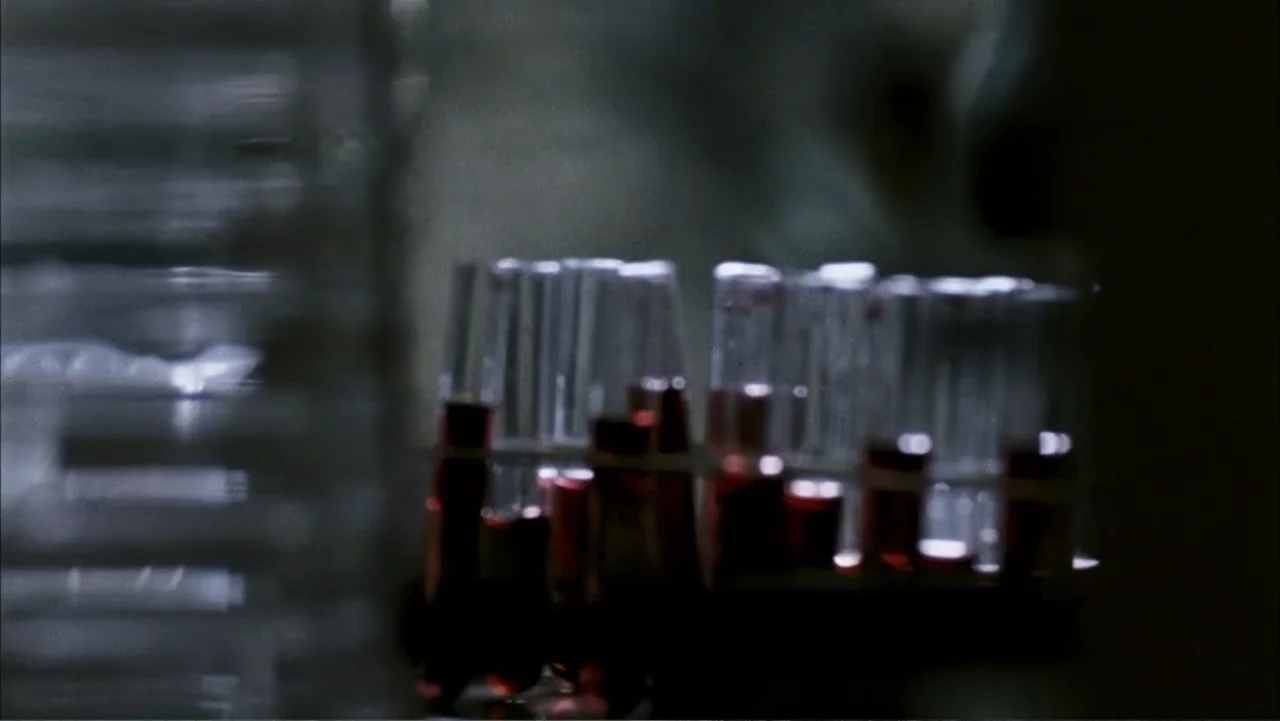 28 Weeks Later (2007) movie still: closeup — A dark laboratory workspace contains a rack of glass test tubes holding red liquid. The tubes are…