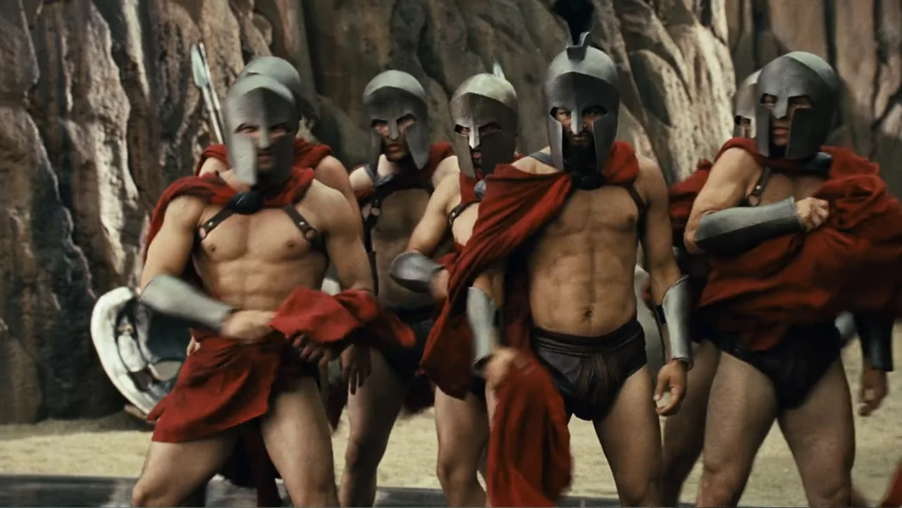 Meet the Spartans (2008) movie still: fullbody — A group of Spartan soldiers stands in a narrow rocky passage with sheer stone walls. The men…