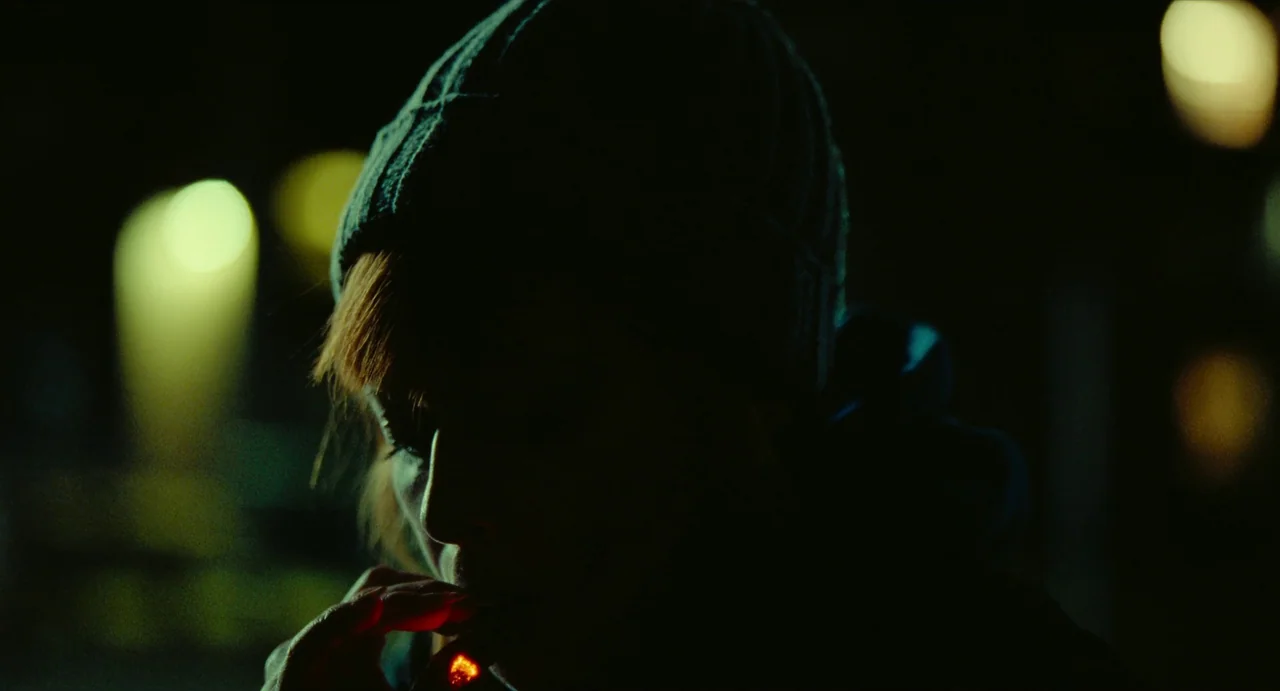 His Three Daughters (2023) movie still: closeup — A dark night setting features out-of-focus street lights glowing in the deep shadows. A woman…