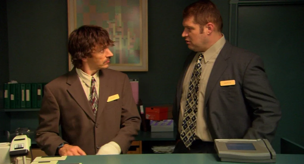 Me and You and Everyone We Know (2005) movie still: medium — An office environment with dark green walls and stacks of files on shelving. Two men in…