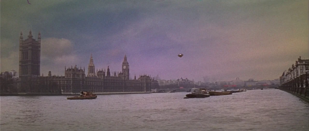 Casino Royale (1967) (1967) movie still: establishing — The Houses of Parliament stand on the bank of the river under a cloudy sky. A small metallic…