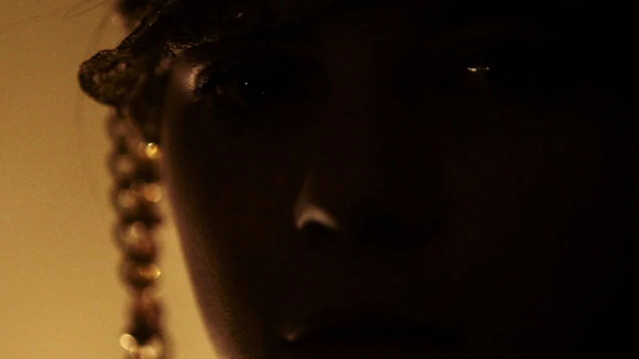 Snowbound (2017) movie still: closeup — A dark indoor space with minimal light focused on a person's partially obscured face. A person looks toward…