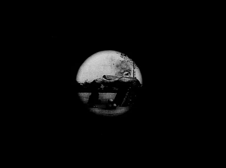 My 20th Century (1989) movie still: fullbody — A circular peephole view shows a person standing next to a large metal cannon. The setting appears to…