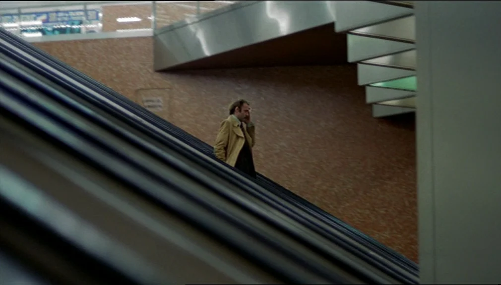 The American Friend (1977) movie still: wide — A modern transit station interior features orange textured wall tiles and metallic structural beams.…