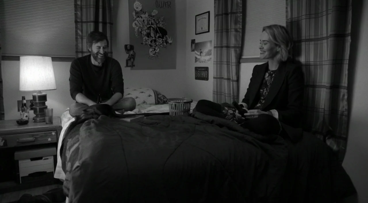Blue Jay (2016) movie still: medium — A bedroom with plaid curtains and a poster on the wall containing a bed. Two people sit on opposite sides of…