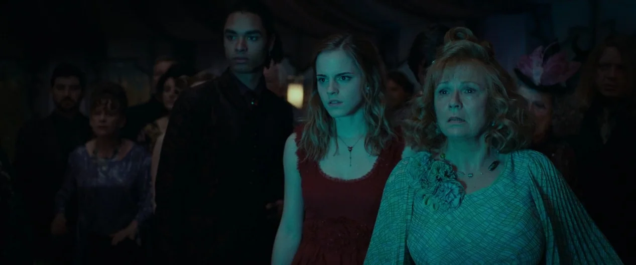 Harry Potter & The Deathly Hallows Part 1 (2010) movie still: medium — A dimly lit indoor gathering with many people in formal attire. The primary…