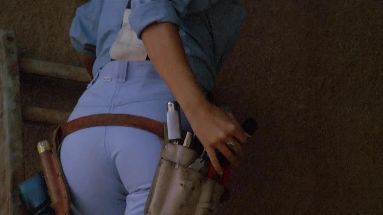 The Slumber Party Massacre (1982) movie still: medium — A person stands against a textured, light brown concrete surface during the day. They wear a…