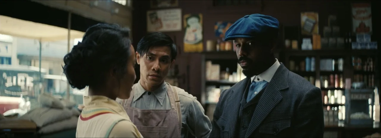Sinners (2025) movie still: medium — A 1930s general store interior contains wooden shelving units filled with canned goods. Three people stand near…