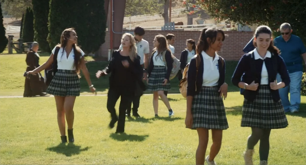 Gates of Darkness (2019) movie still: fullbody — A sunny grassy quad is flanked by a low brick wall and a fence. Several teenagers wearing uniforms…