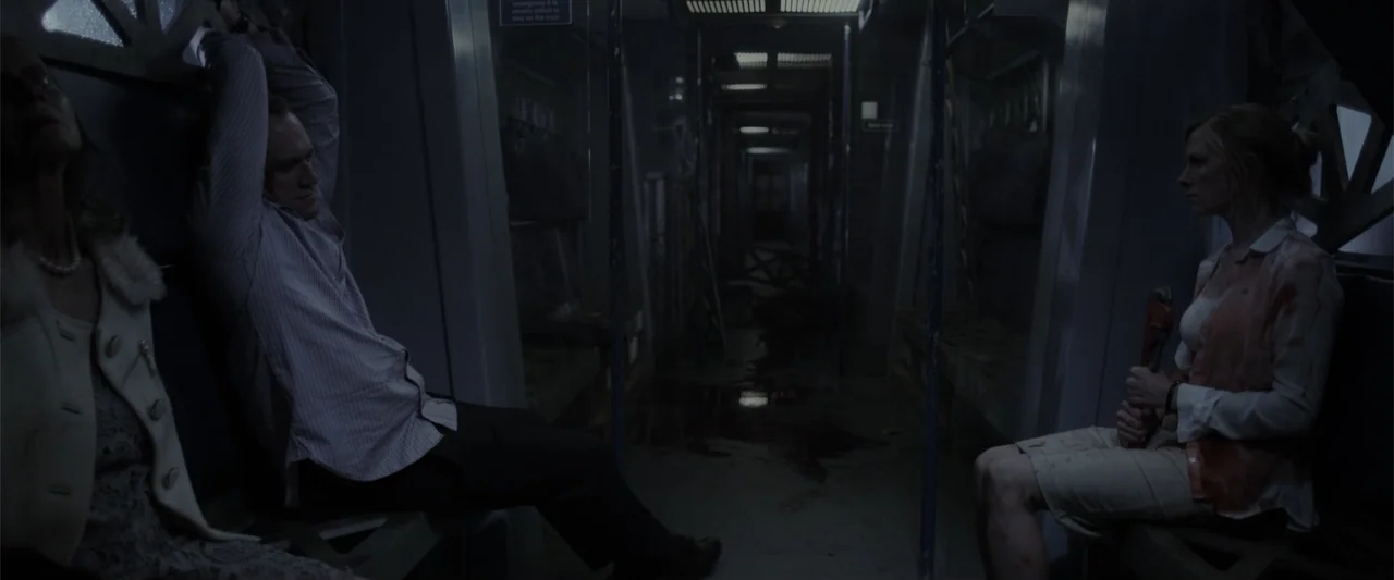 Howl (2015) movie still: wide — A dimly lit subway car interior with rows of empty seating and metal poles. Three people sit separated across the…