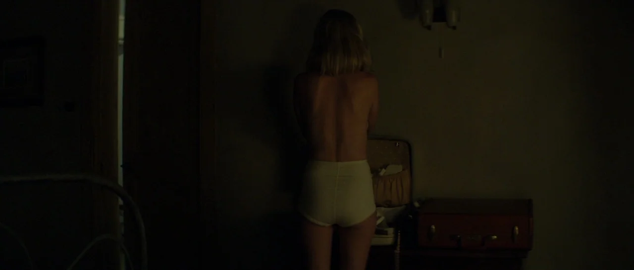 The Two Faces of January (2014) movie still: medium — A dimly lit room contains a suitcase placed on a surface against a wall. A woman stands in…