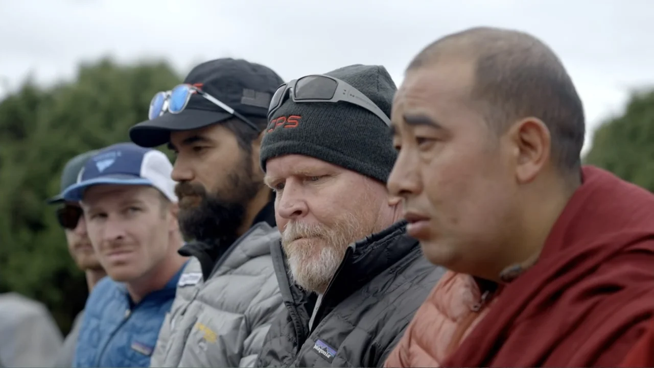 Drop Zone Everest (2023) movie still: medium — A group of diverse men stands outdoors on a cloudy day. The subjects are arranged in a line looking…