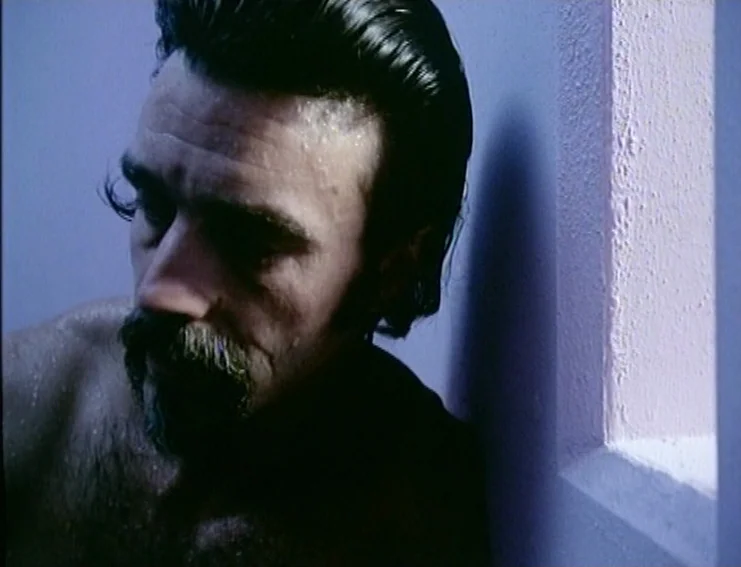 Ghosts… Of The Civil Dead (1988) movie still: closeup — A man with a mustache and slicked-back hair leans against a wall. Water droplets cover his…