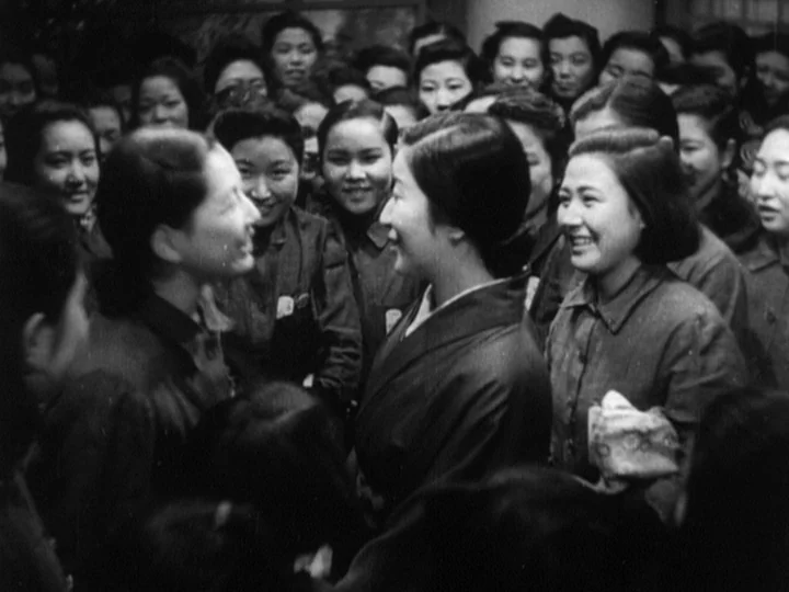 The Most Beautiful (1944) movie still: medium — A crowded indoor space is filled with numerous women in a dense cluster. Two central figures face…