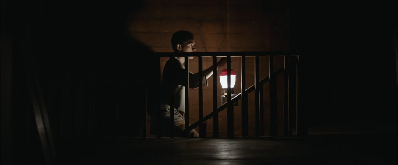 It Comes at Night (2017) movie still: medium — A dark wooden staircase features vertical railings in the foreground and a stone-textured wall. A…