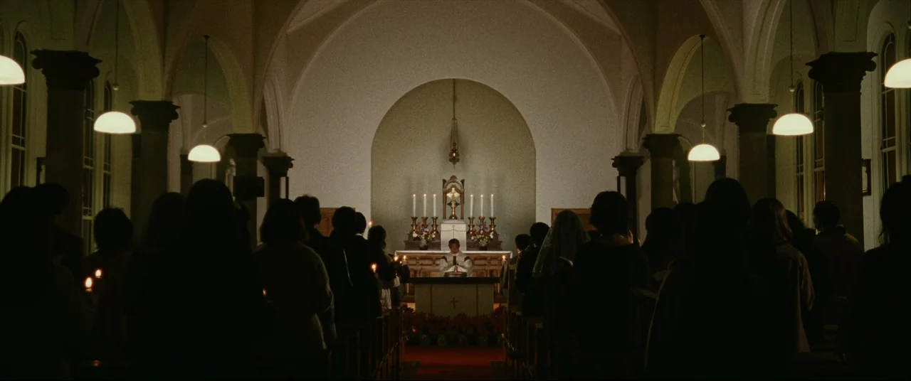 The World of Kanako (2014) movie still: wide — A dimly lit church interior with rows of people seated in dark pews. At the front stands an altar…