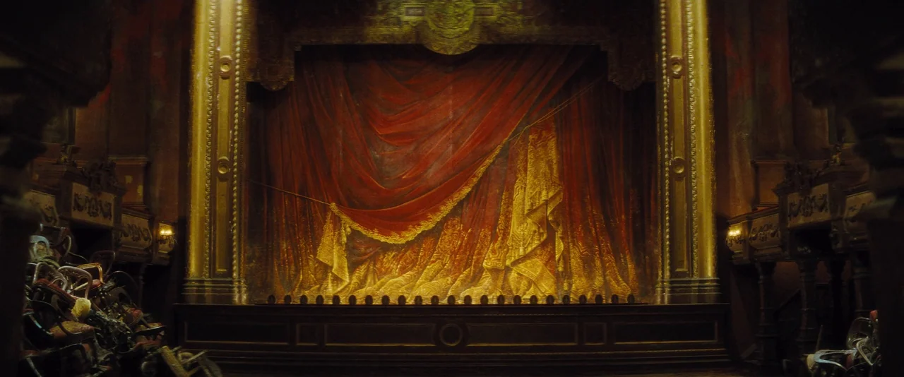 Anna Karenina (2012) movie still: establishing — An ornate interior of an aged theater features a central stage hidden by heavy red velvet curtains.…