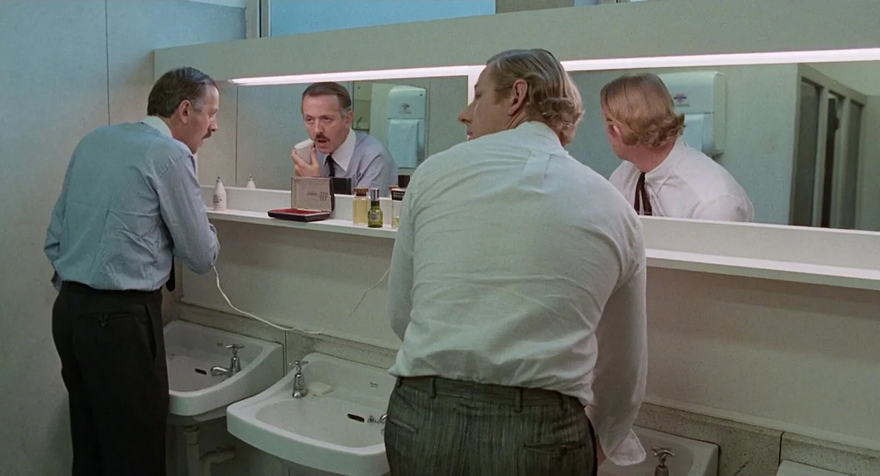 Quadrophenia (1979) movie still: medium — A sterile public washroom features white tiled walls and a long horizontal vanity mirror. Two men stand at…