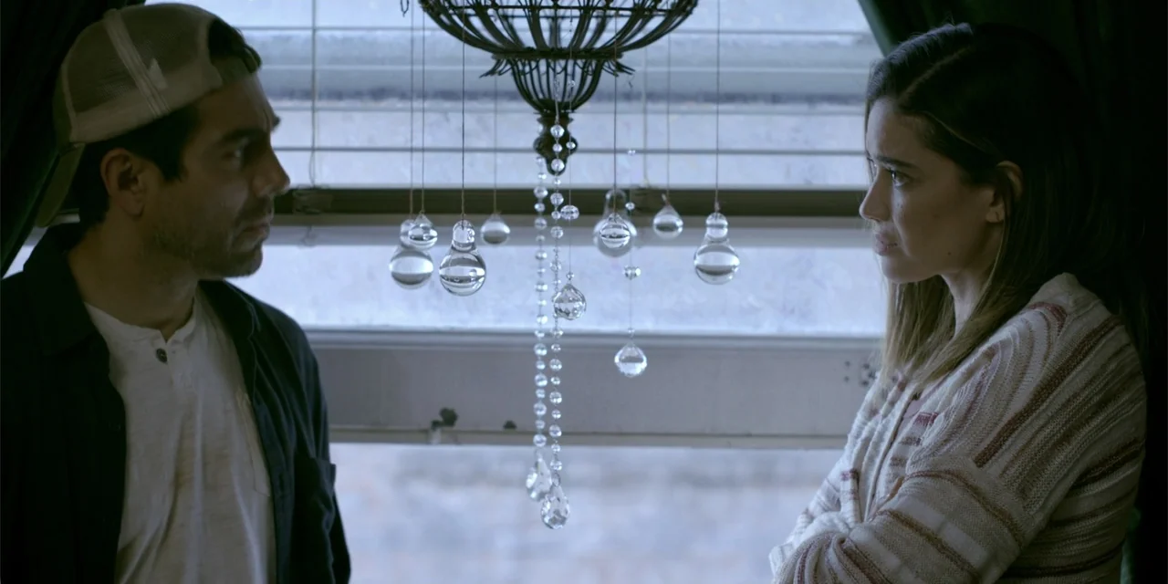 7th & Union (2021) movie still: medium — A residential interior features a window with horizontal blinds and a hanging crystal ornament. A man…