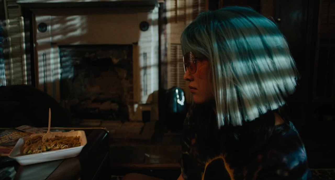 Mona Lisa and the Blood Moon (2022) movie still: medium — A dimly lit room features a fireplace in the blurred background. A young person with blue…