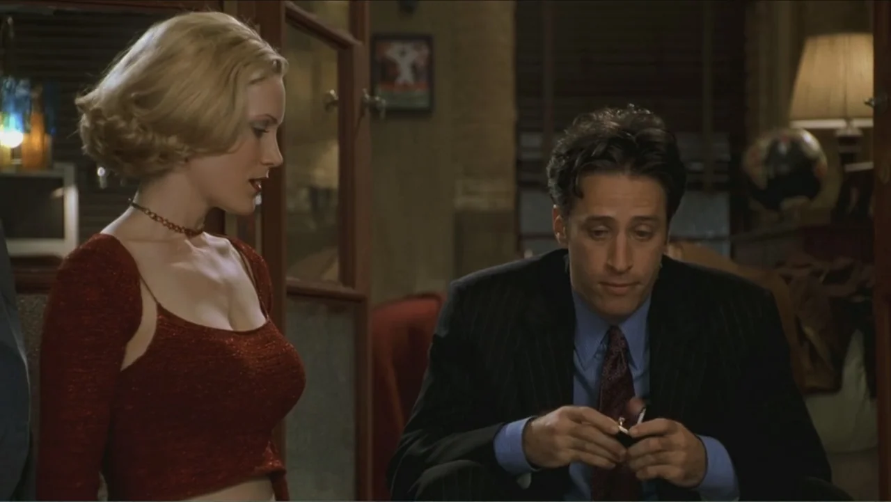 Big Daddy (1999) movie still: medium — A furnished apartment interior with a lamp and dark wooden shelving in the background. A man kneels while…