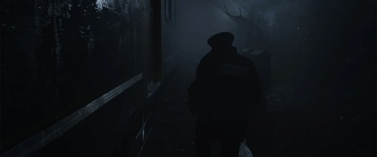 Howl (2015) movie still: medium — A dark outdoor platform features a stationary passenger train car beside a shadowed pathway. A lone figure in a…